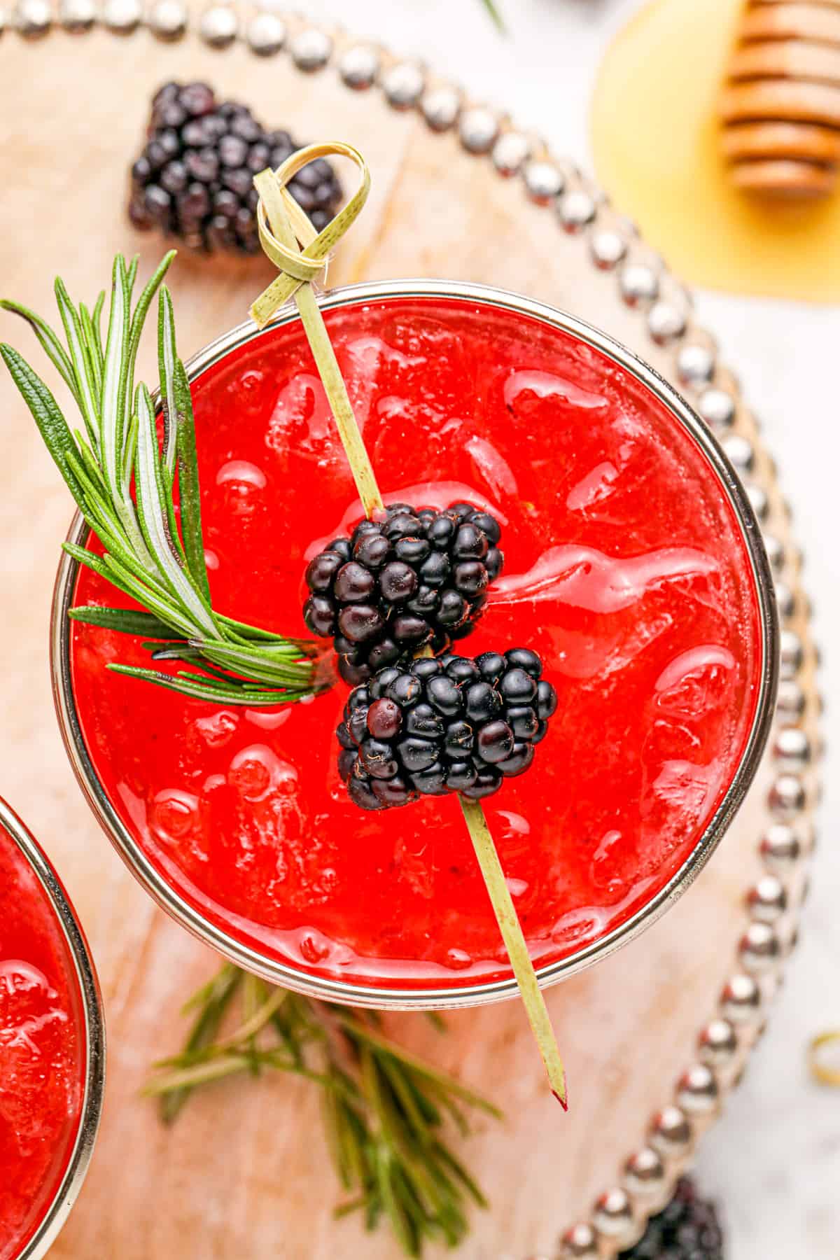 Overhead of a Blackberry Bourbon Smash on wooden tray garnished with blackberries and thyme with other ingredients around glass.