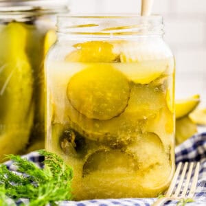Close up square image of pickles in jar with fork and a jar of pickle spears behind it.
