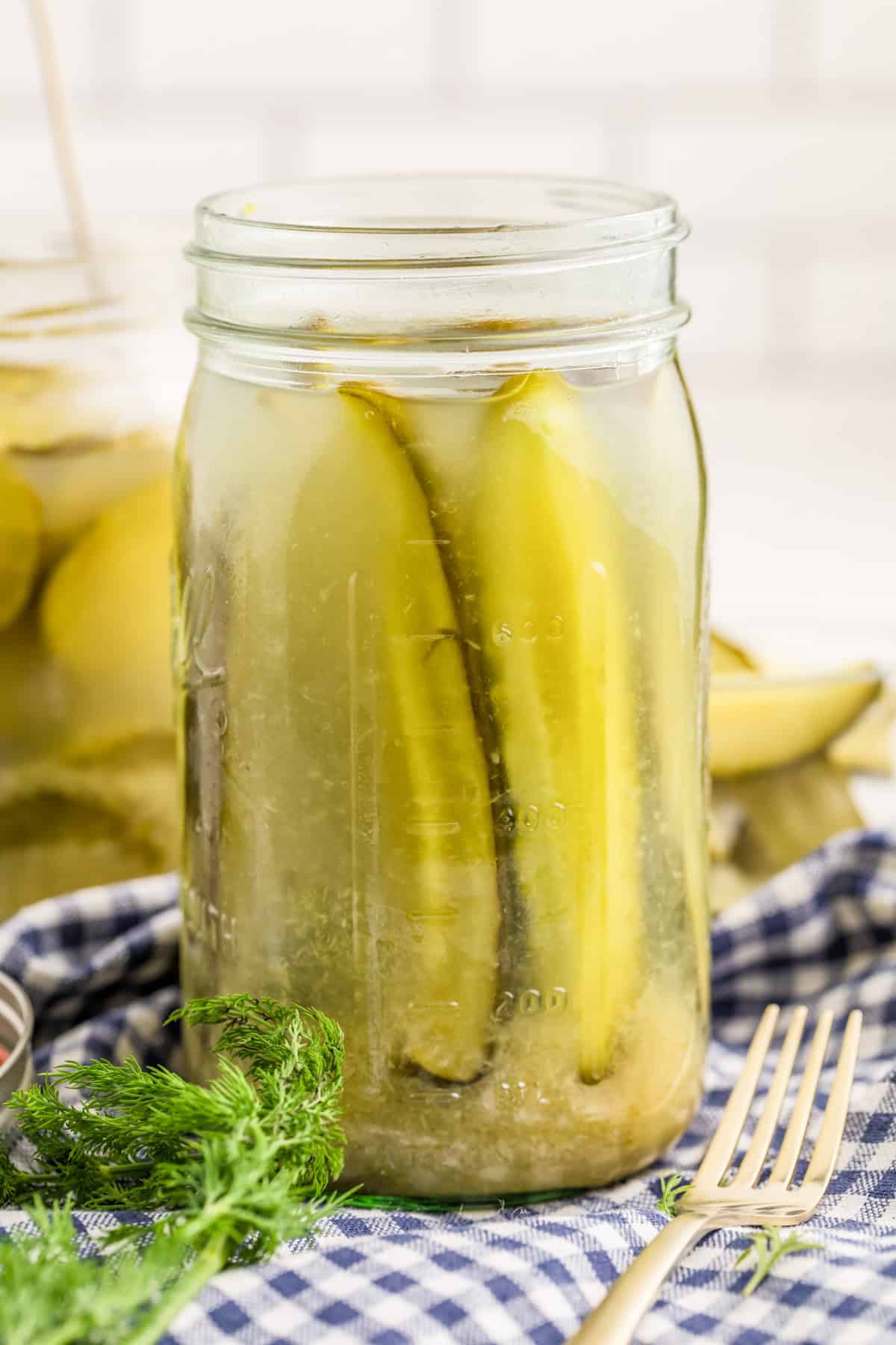 Horseradish Pickle spears in jar with fork and herbs in front of jar.