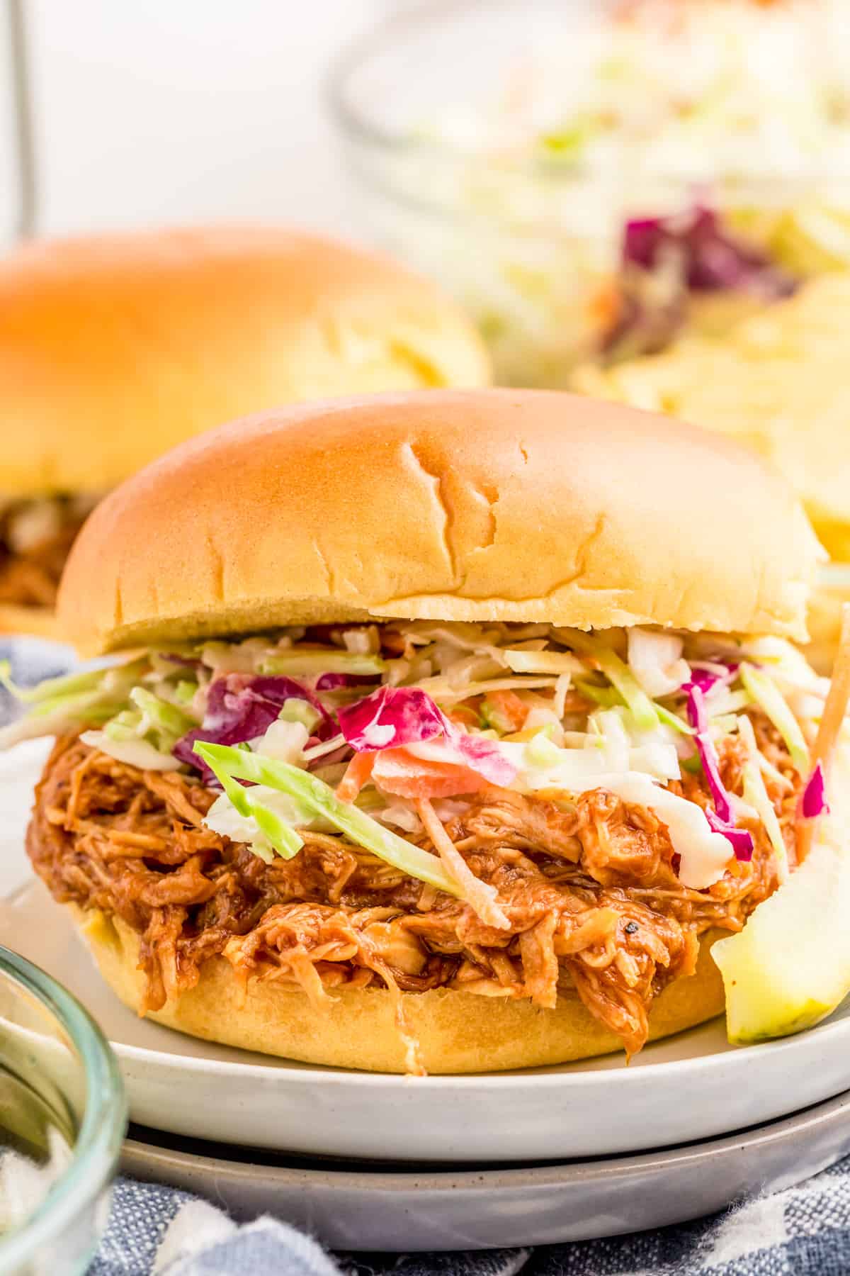 Slow Cooker BBQ Chicken served on a sandwich topped with coleslaw on stacked white plates.