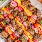 Close up square image of finished Kabobs on white plate topped with parsley.
