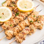 Close up of chicken finished on white plate garnished with herbs and lemon slices.