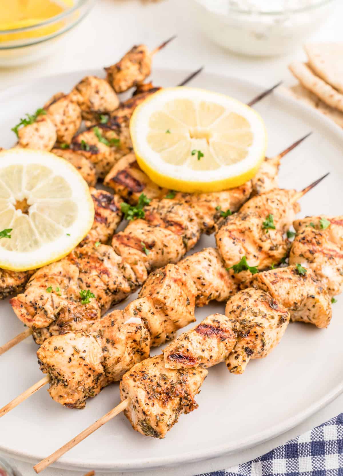Finished Chicken Souvlaki on white plate garnished with herbs and lemon slices.