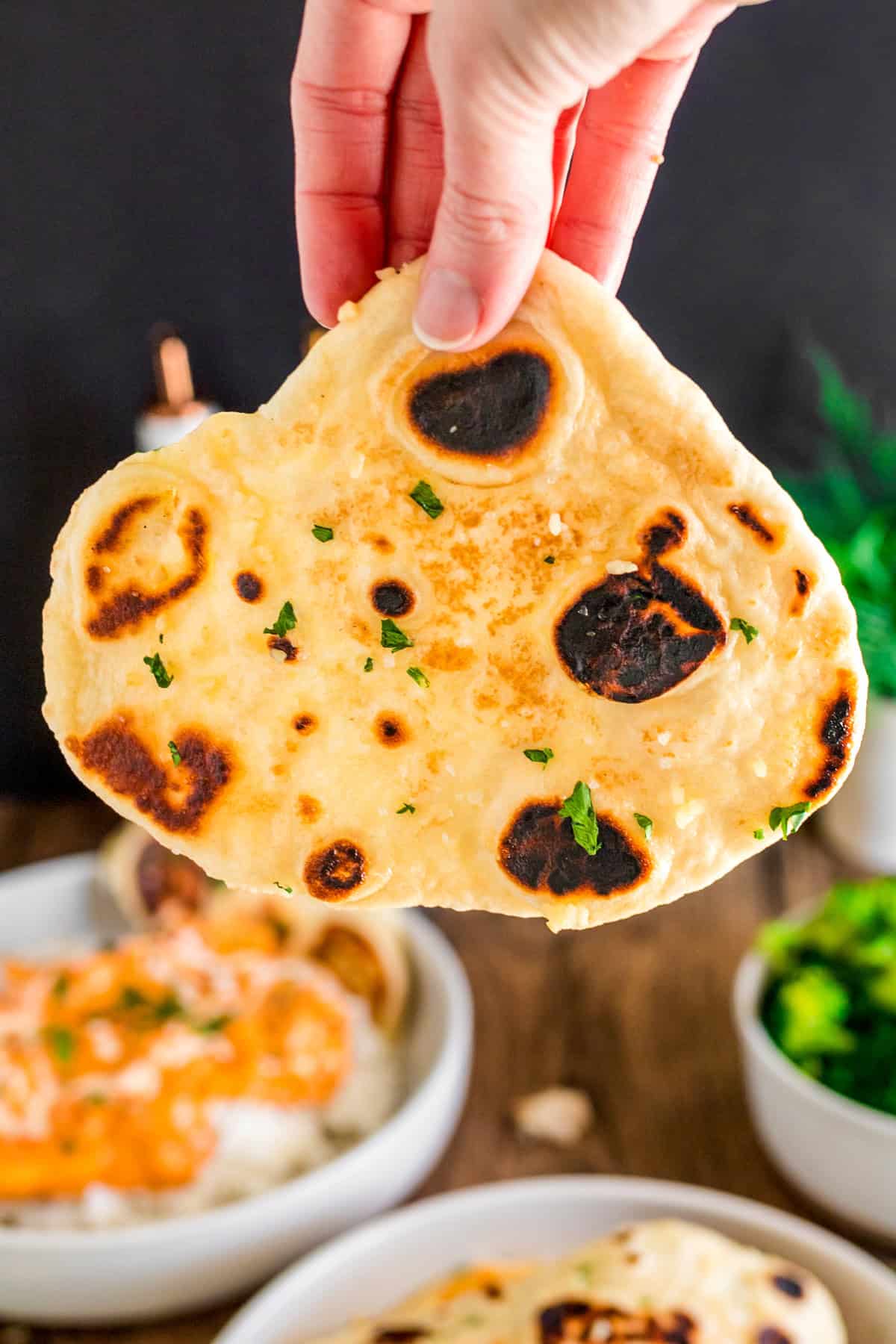 Hand holding up a piece of Garlic Naan showing the char marks.