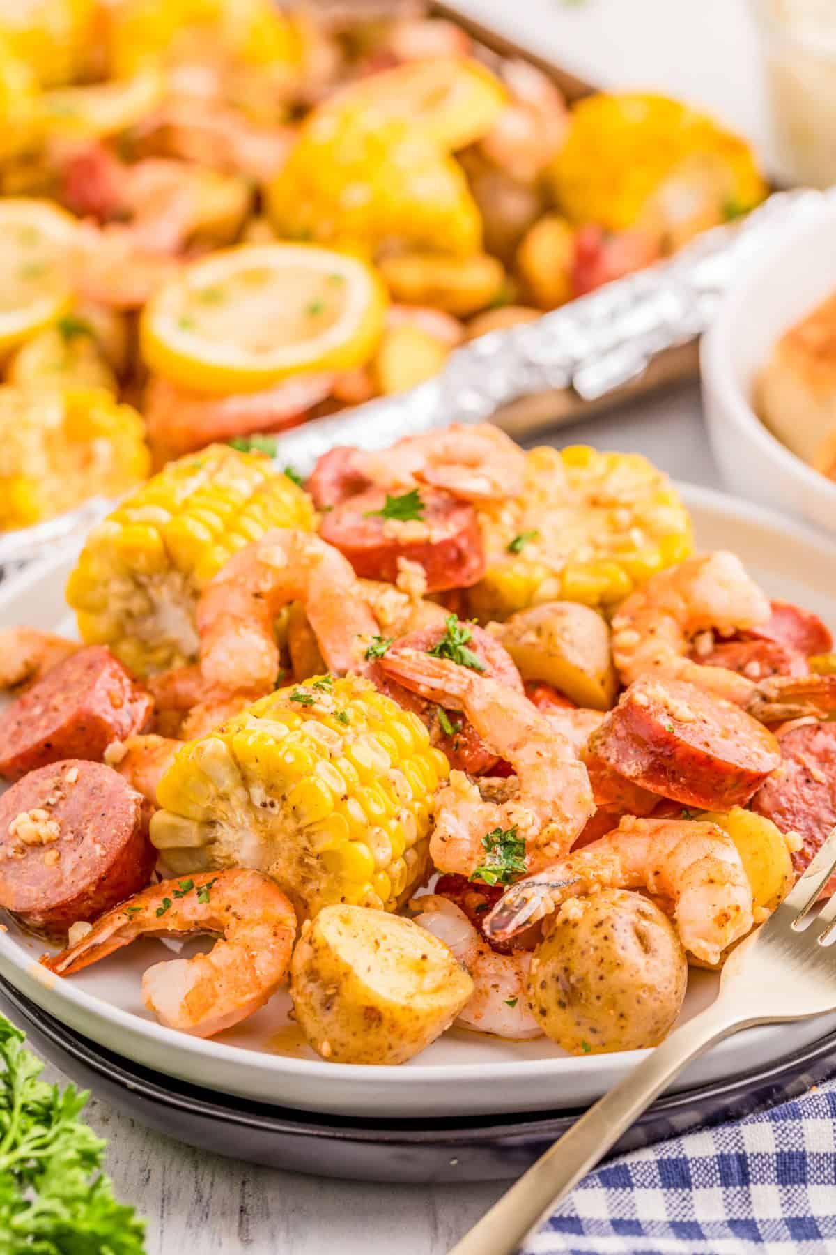 Sheet Pan Shrimp Boil on a plate with the pan in the background. Plate layered with all the boil ingredients.