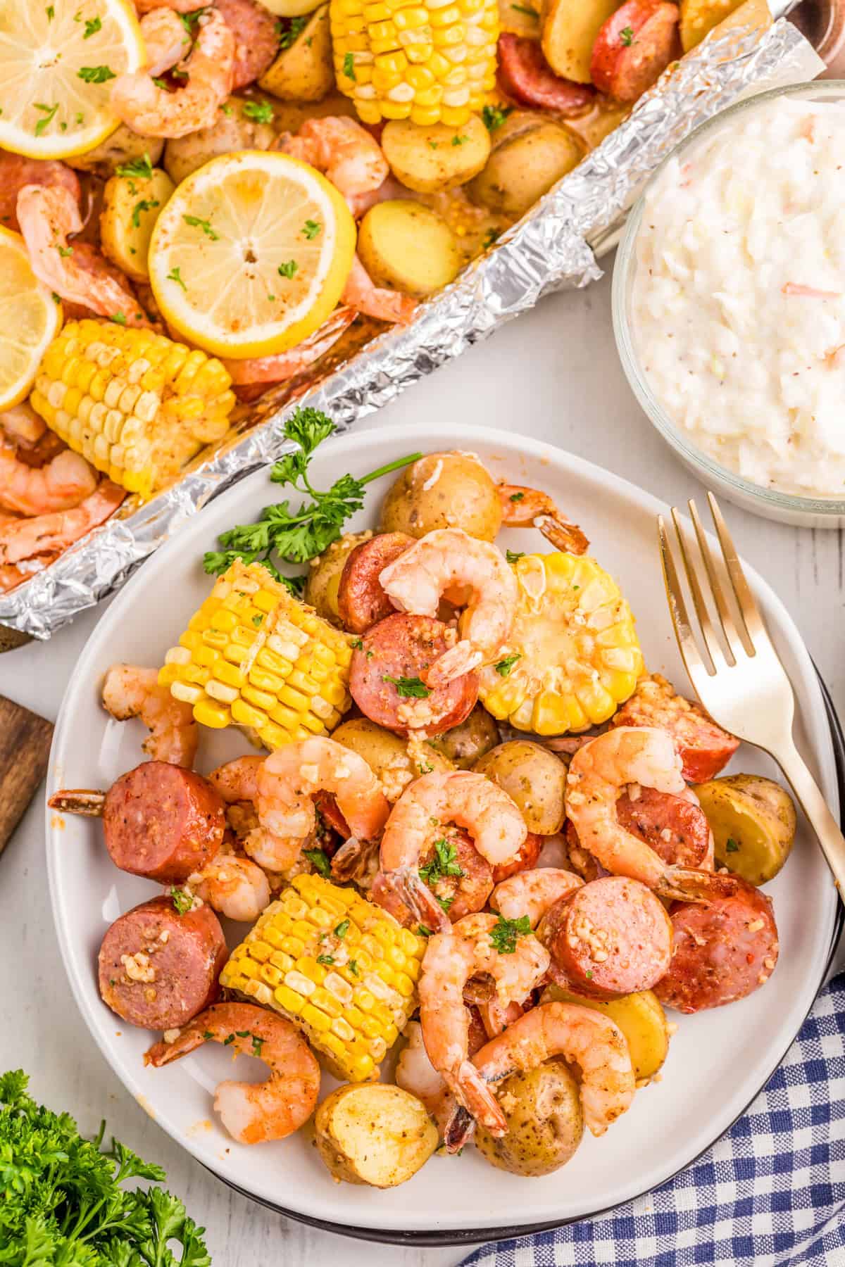 Overhead of Shrimp Boil on white plate with fork and cole slaw with sheet pan next to plate.