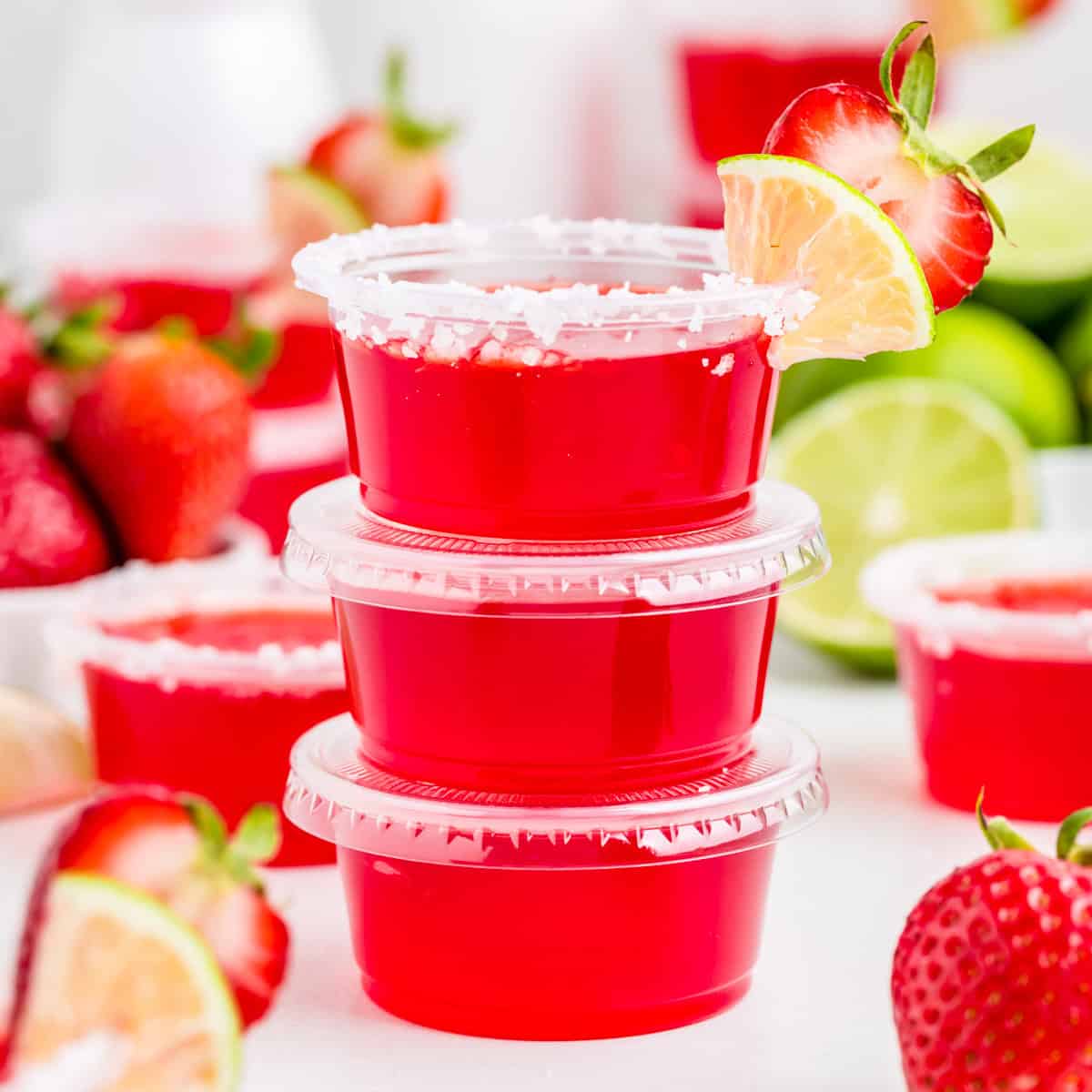 Close up of three Jello Shots stacked on top of one another with top one garnished with salt, lime and strawberry.