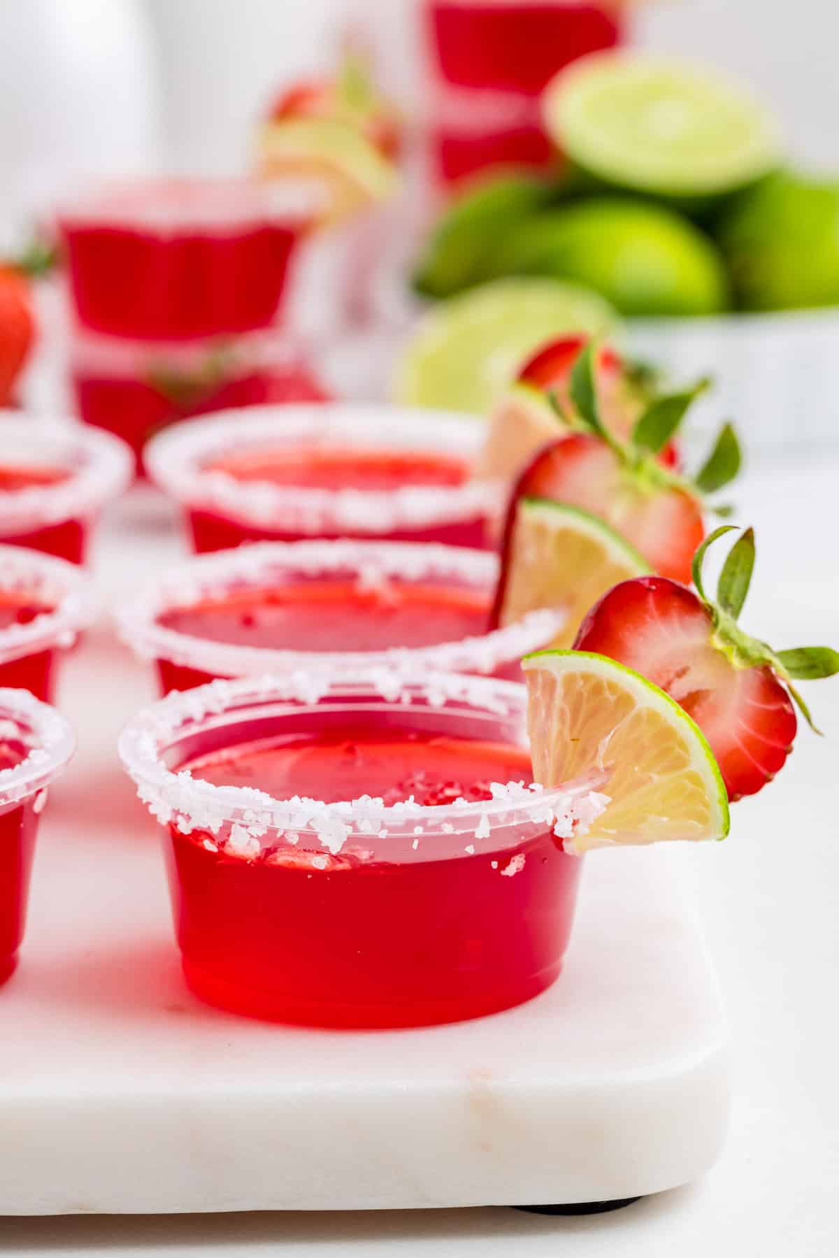 Shots lined up in a row showing off their salt, lime and strawberry garnishes.
