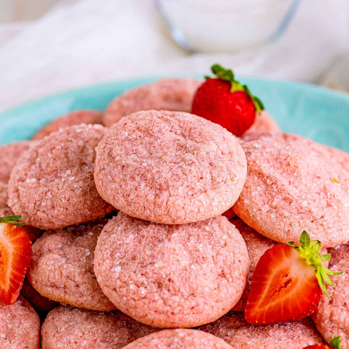 Square image of cookies stacked on top of one another on a blue plate with strawberries.