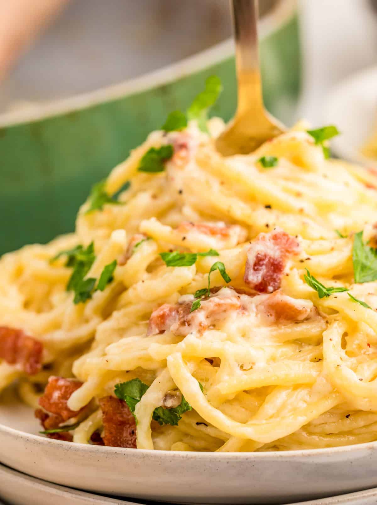 Close up of pasta on white plate showing the creamy sauce and bacon with fork sticking out of the top.