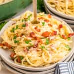 Square image of pasta on plate garnished with bacon and parsley with fork sticking out from center.