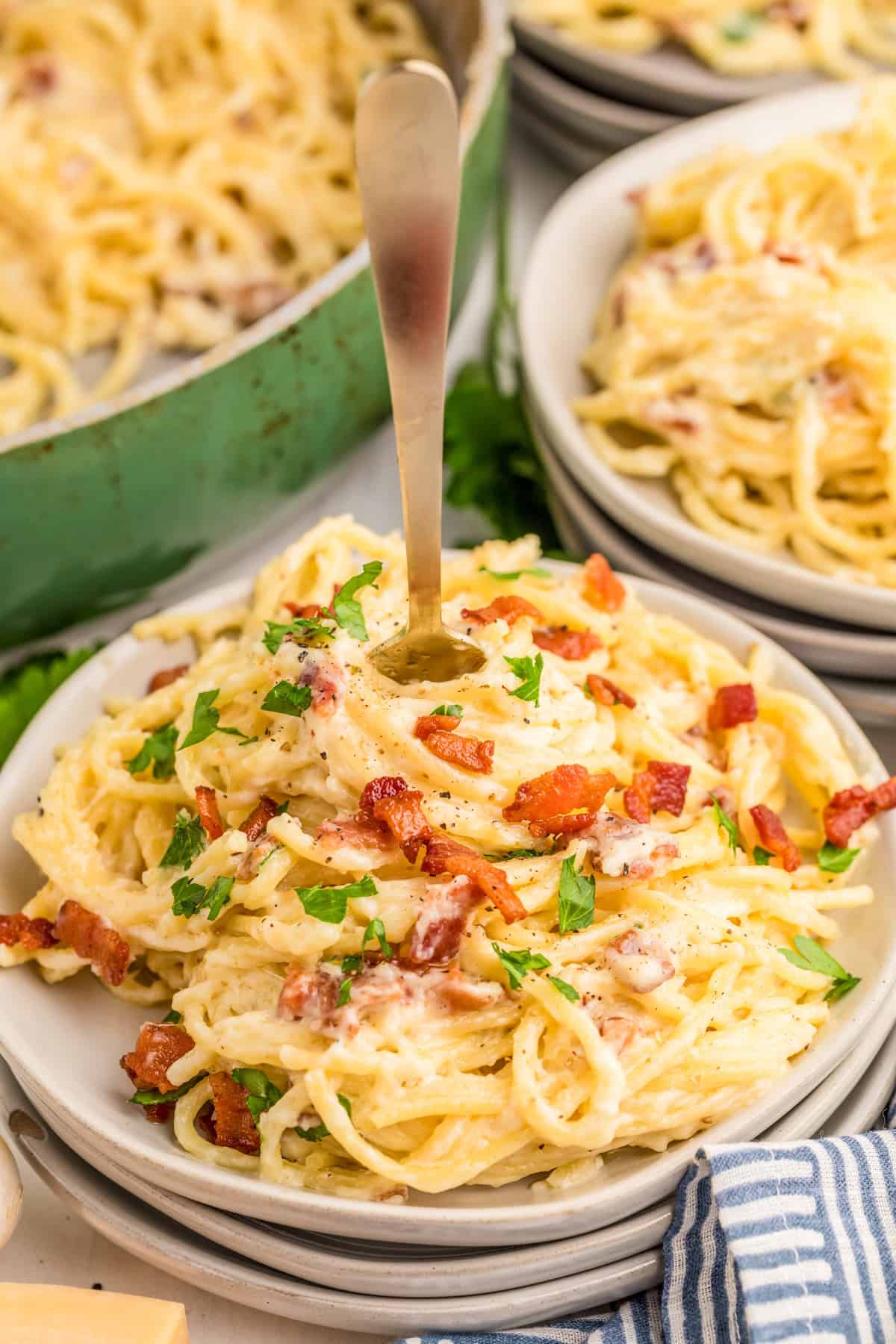Bacon Pasta on stacked white plates topped with bacon and parsley with a fork in the center of the pasta.