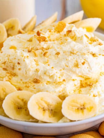 Close up square image of dip in white bowl with sliced bananas and crushed vanilla wafers/