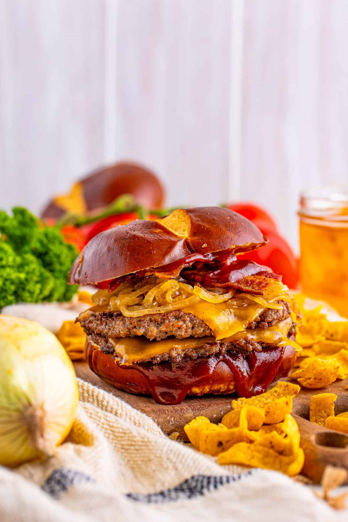 BBQ Burger on wooden serving board surrounded by Fritos and other ingredients.