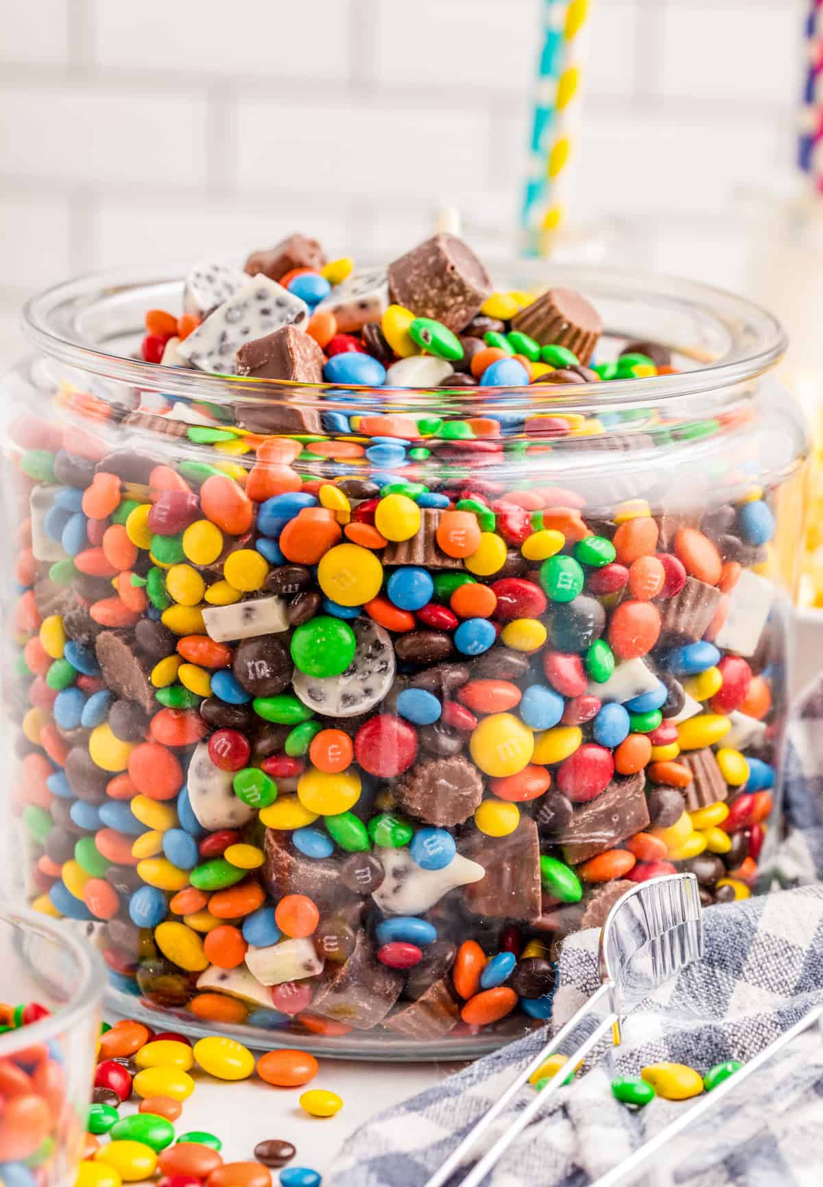 Chocolate Candy Salad in a large glass container with tongs and candy beside bowl.