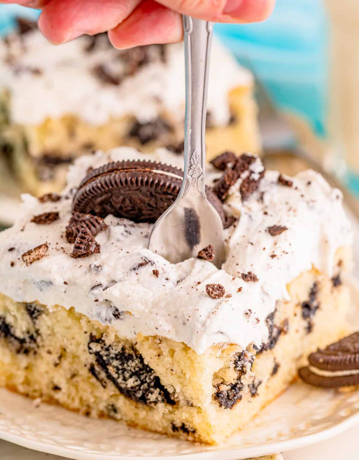 Close up of a fork going into a slice of cake on a white plate.