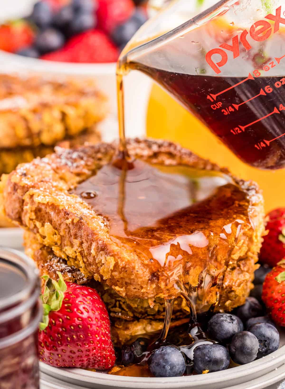 Syrup being poured over stacked french toast on plate with fruit.