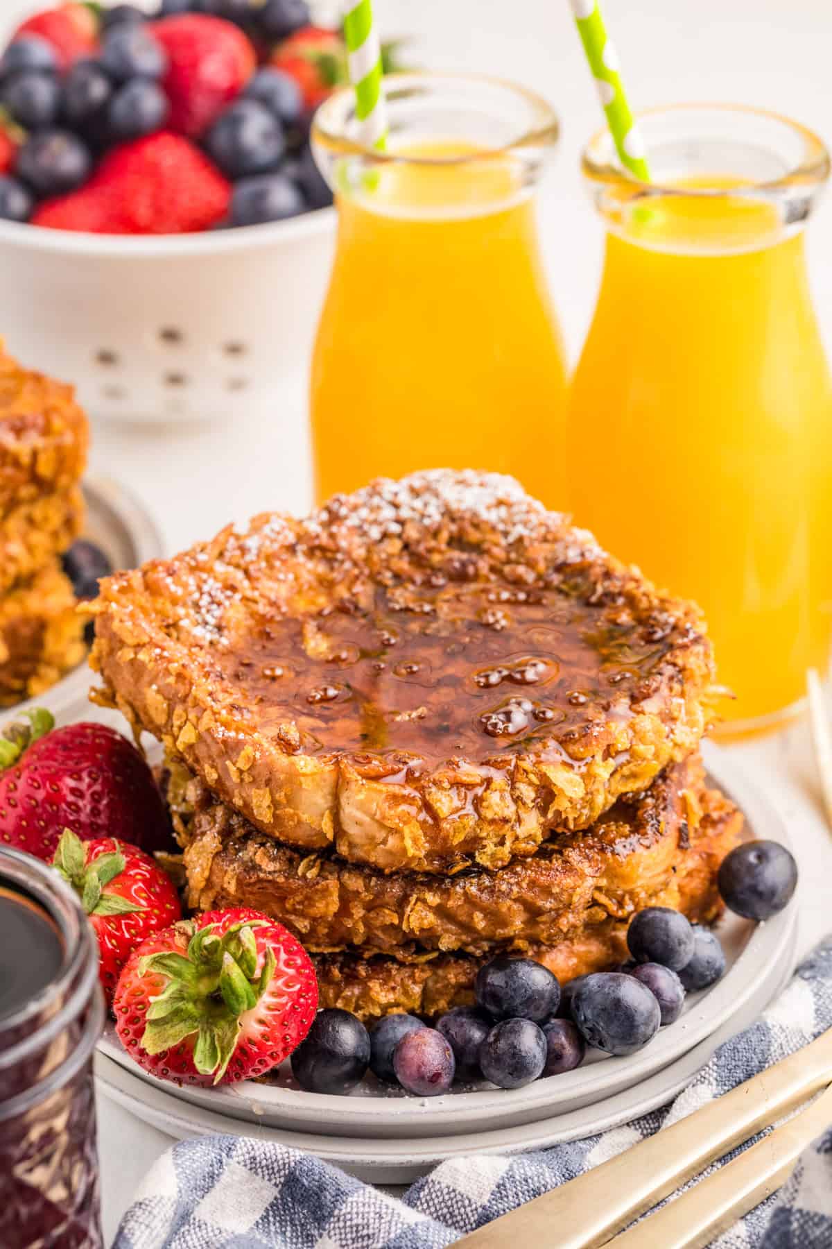 Crunchy French Toast stacked on white plate with fruit and orange juice in background.
