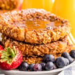 Close up square image of stacked french toast with syrup and fruit on white plate.