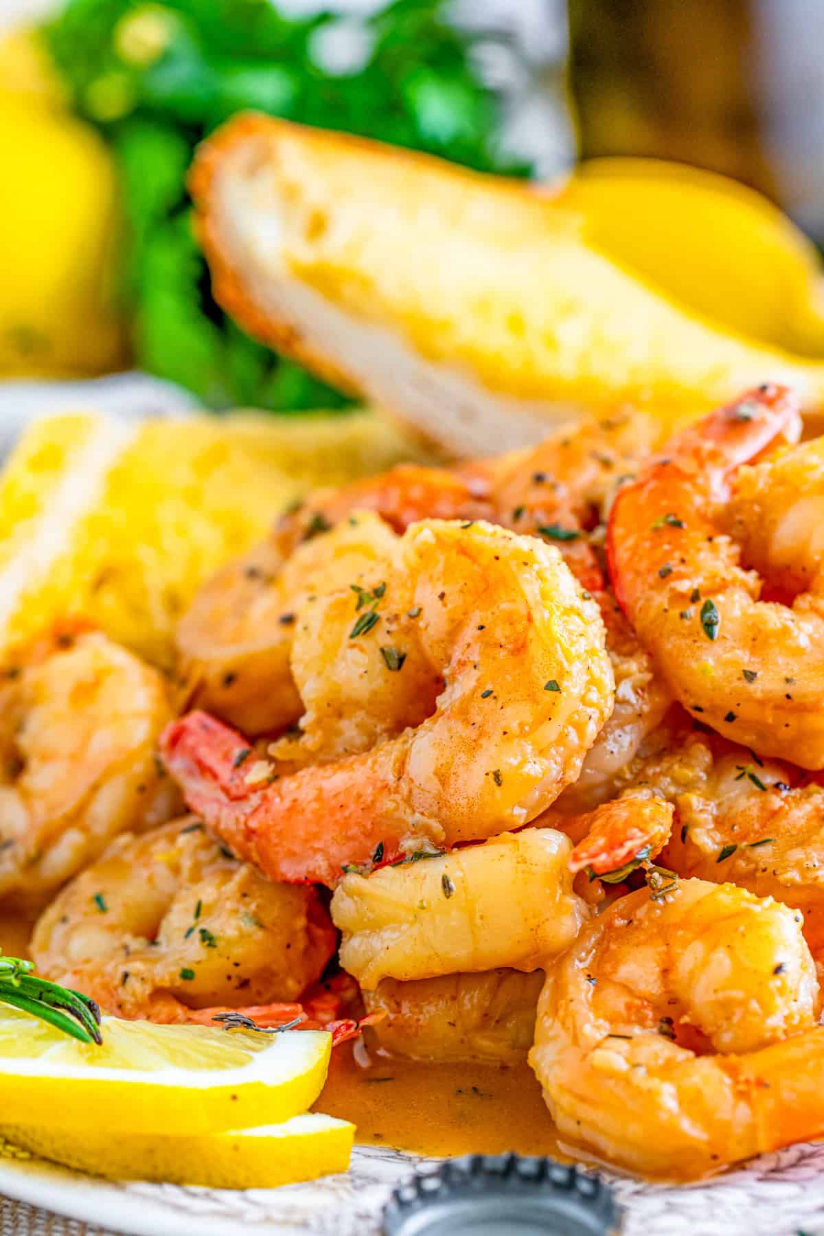 Close up side view of stacked New Orleans BBQ Shrimp on plate with sauce, lemons and garlic bread in back.