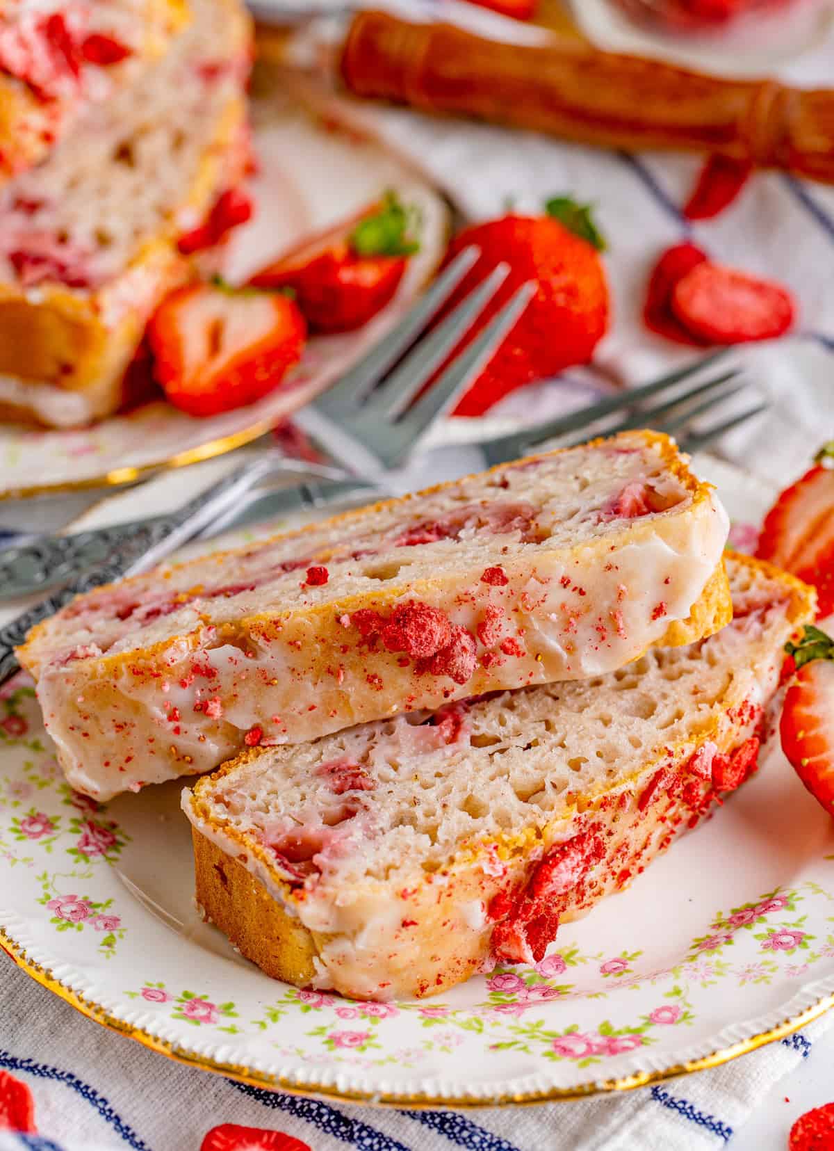 Slices of Strawberry Ice Cream Bread on decorative plate with forks and strawberries around it.