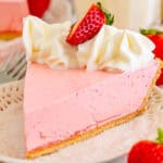 Close up square image of one slice of pie on white plate topped with whipped topping and a sliced strawberry.