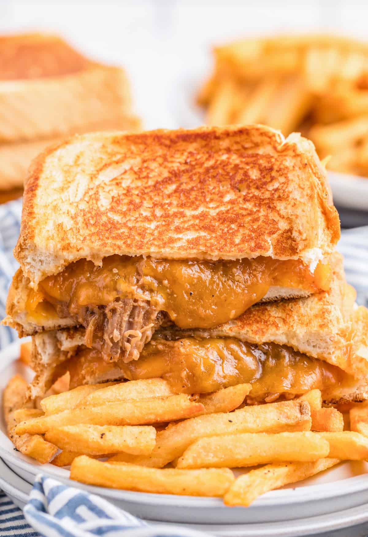 BBQ Pulled Pork Grilled Cheese cut in half showing melty cheese on top of a plate of french fries.