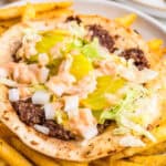 Close up square image of finished taco on plate of fries with toppings.