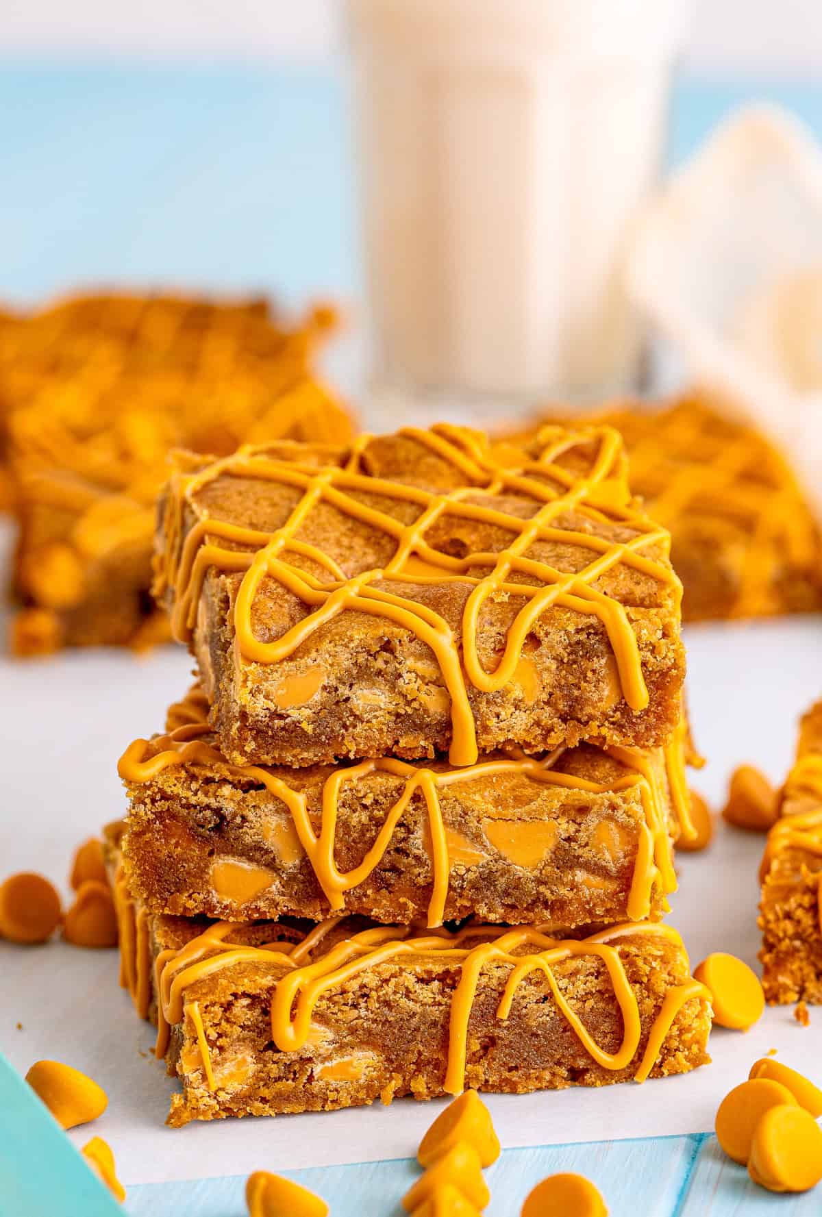 Three Butterscotch Blondies stacked on top of one another with butterscotch drizzle and milk in background.