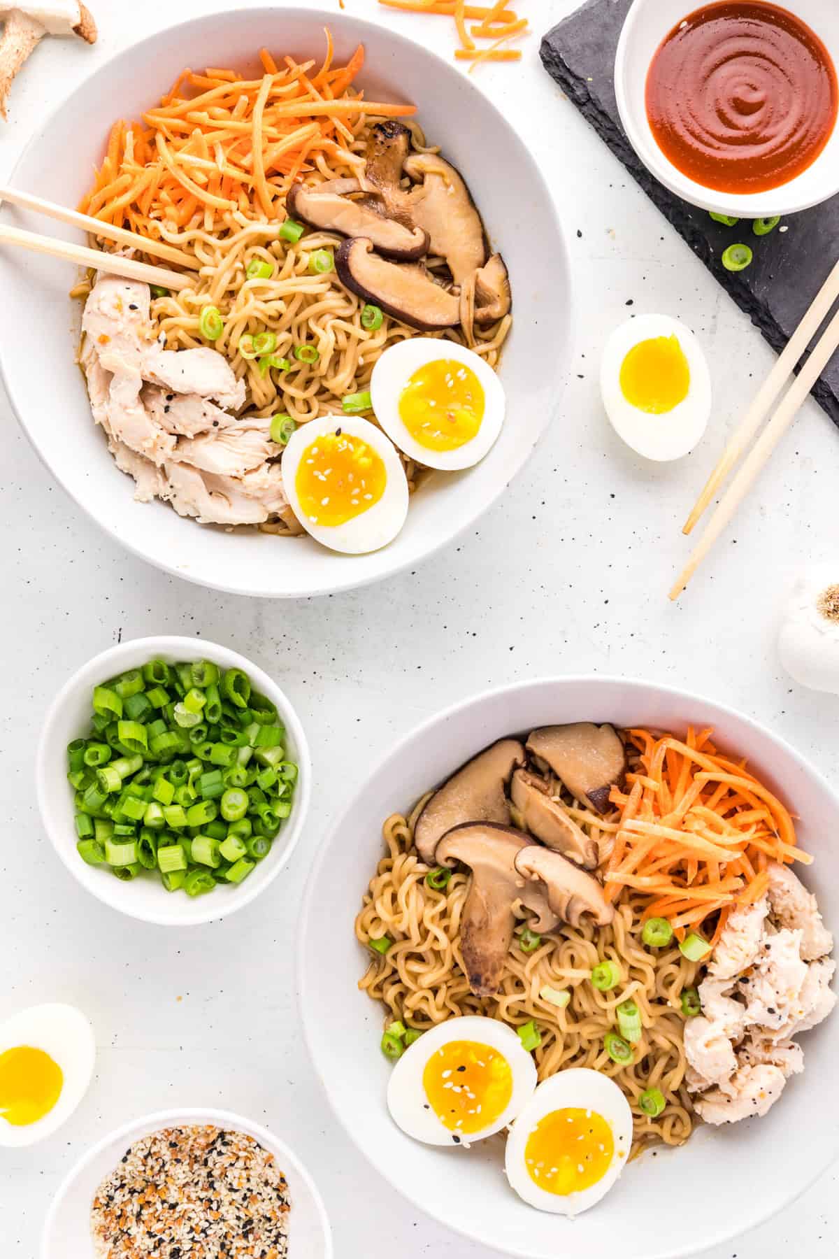 Two bowls of Chicken Ramen overhead with chopsticks, and garnishes around bowls.