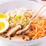 Close up square image of ramen in white bowl with chopsticks.