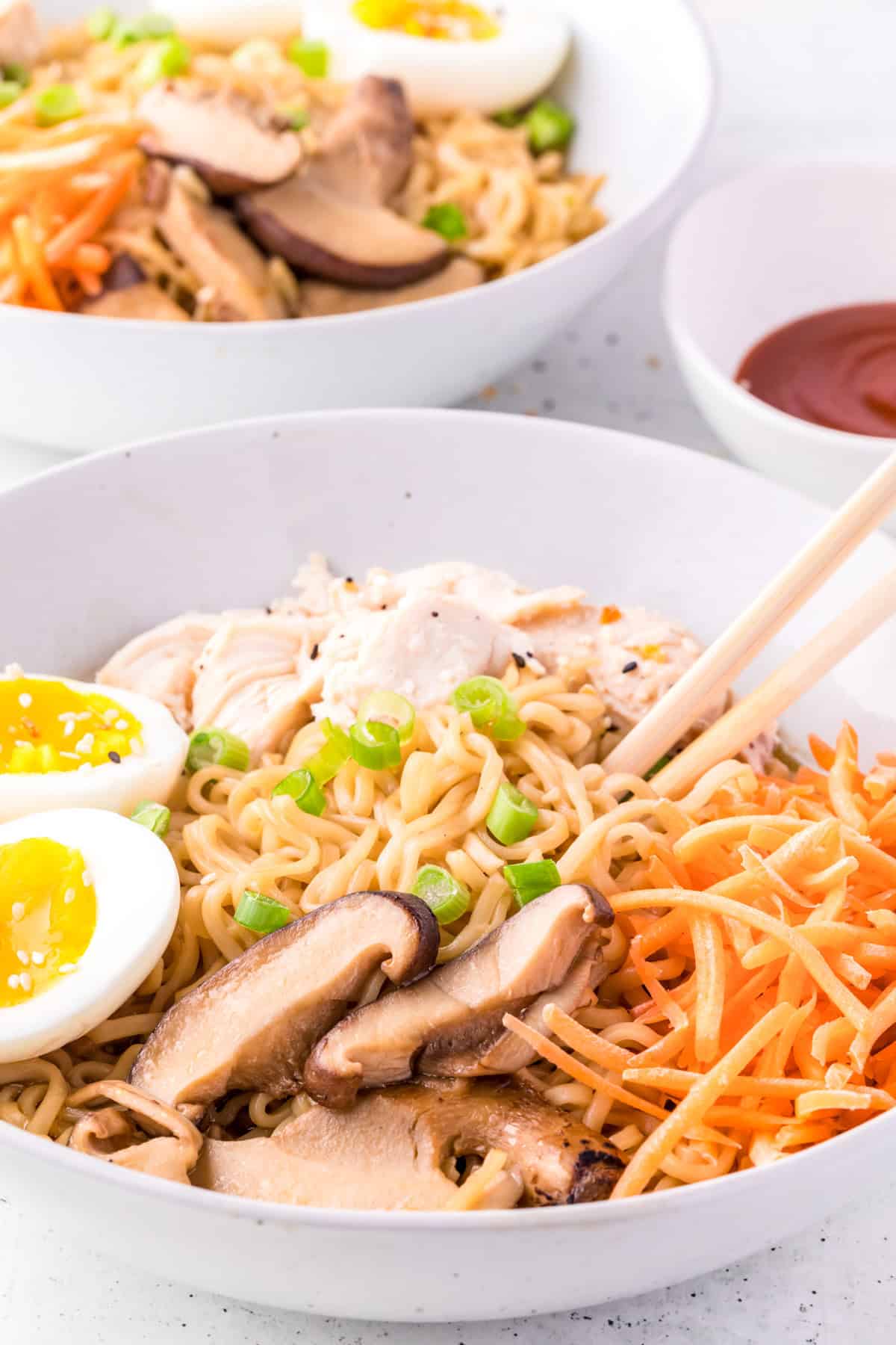 Chicken Ramen in white bowl with chopsticks in bowl and another bowl of ramen in background.