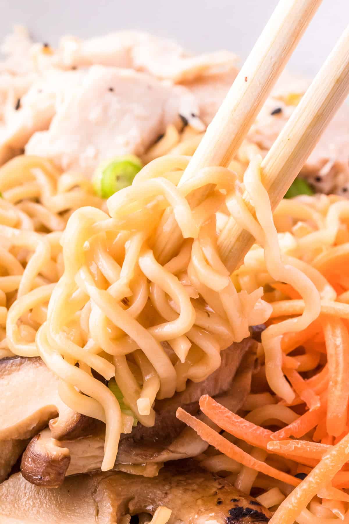 Close up of chopsticks holding up some ramen out of bowl.