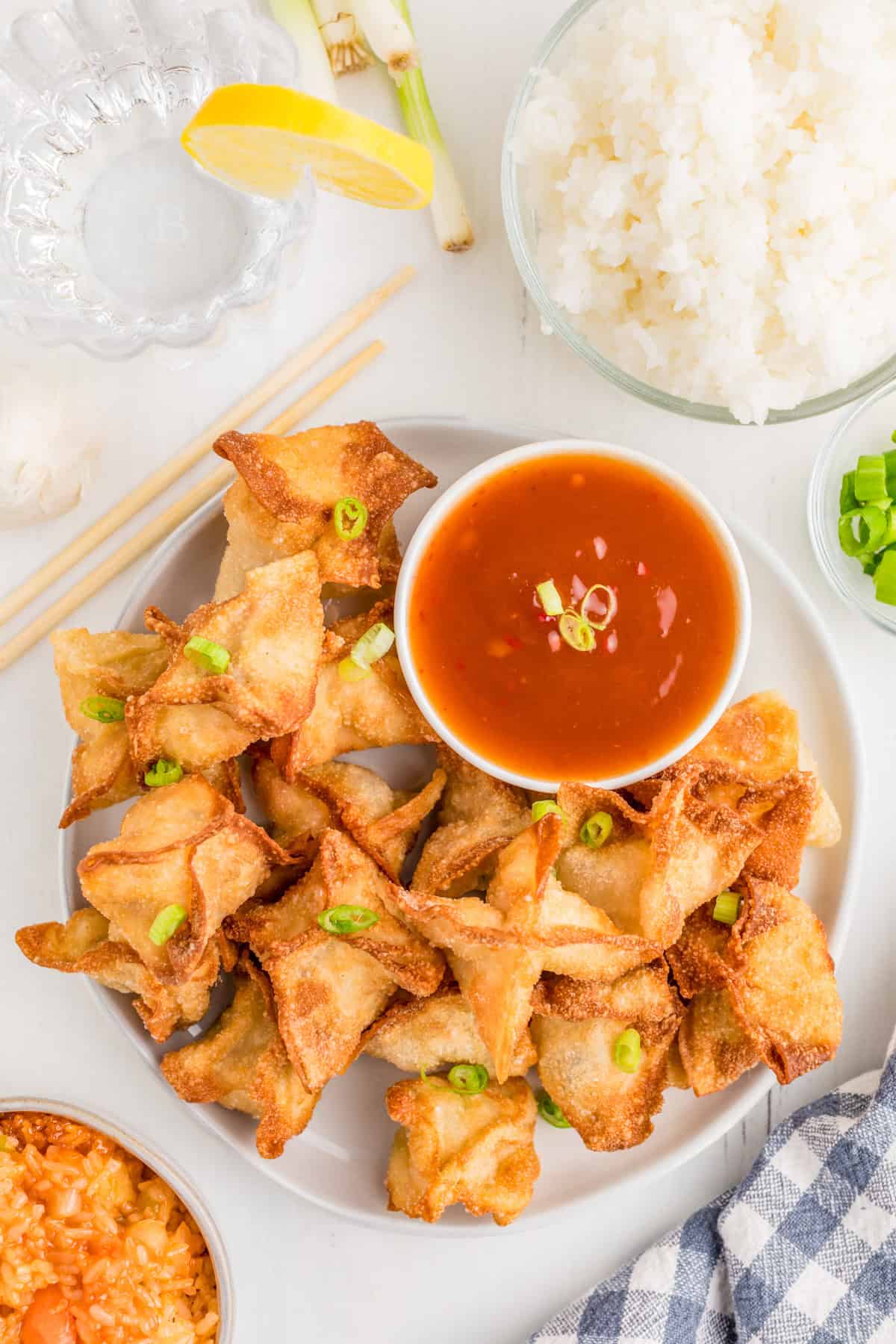 Overhead photo of garnished rangoon on white plate with dipping sauce and rice next to plate.