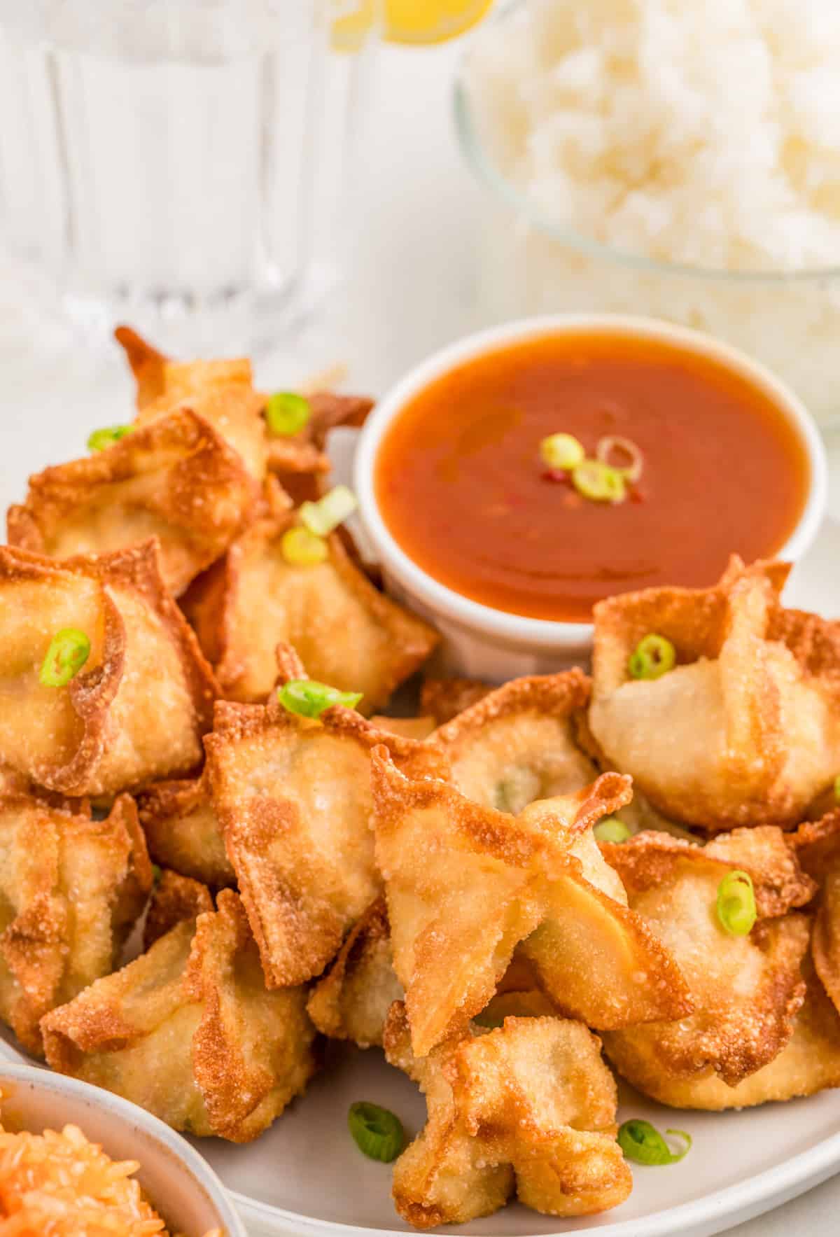 Crab Rangoon on white plate garnished with green onions with dipping sauce in bowl on plate.