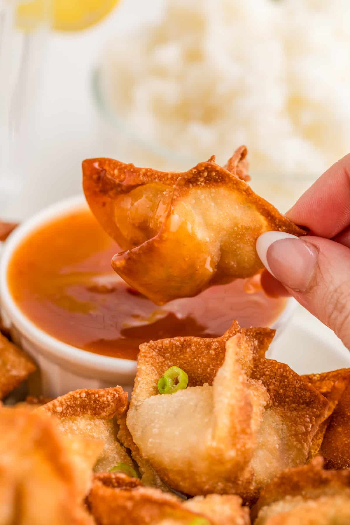 Hand holding up one of the rangoons after its been dipped in the dipping sauce.