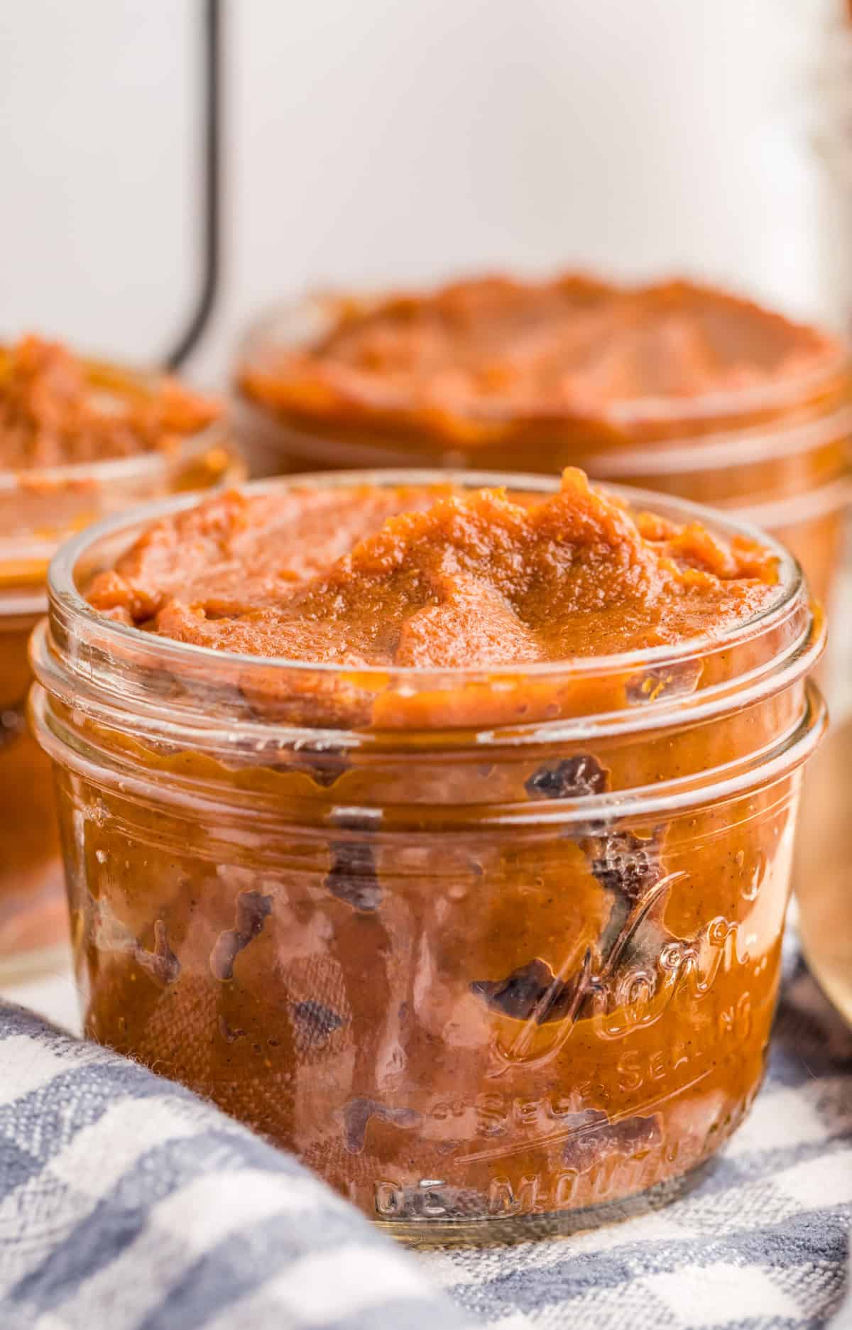 Slow Cooker Pumpkin Butter in glass jar with a white and blue dish towel in front of slow cooker.