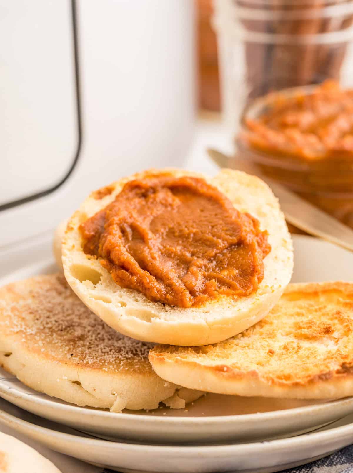 Stacked english muffins on white plate with a half of an english muffin spread with the butter on top.