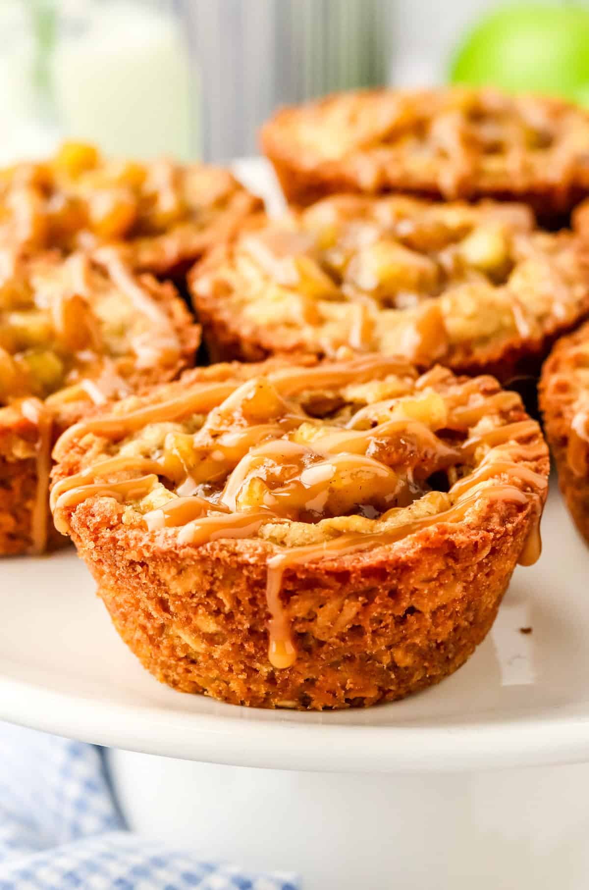 Apple Crisp Cookie Cups on white stand drizzled with caramel.