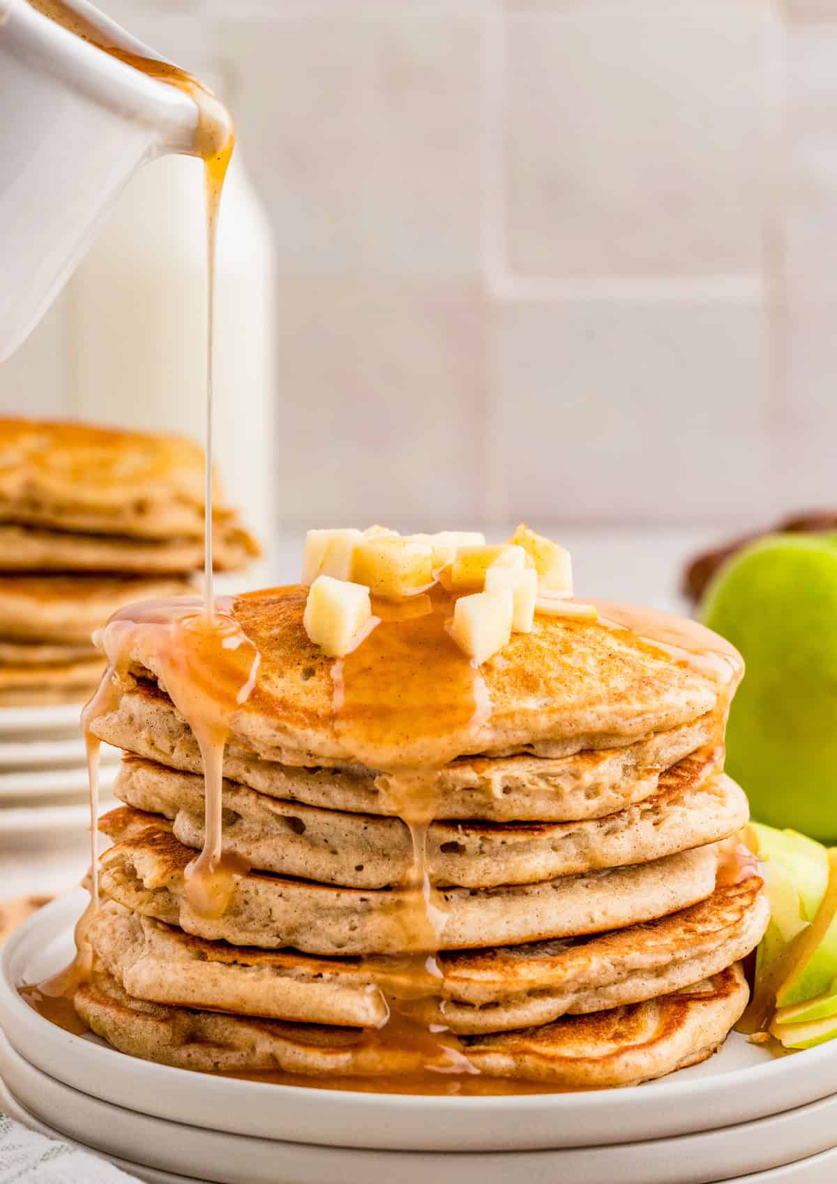 Pancakes stacked on plate getting poured with syrup.