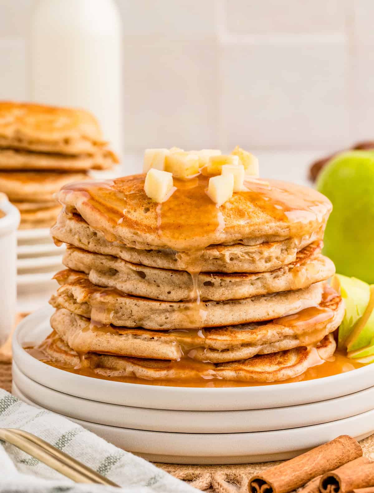 Stacked Apple Pancakes on white plates topped with diced apples and syrup.