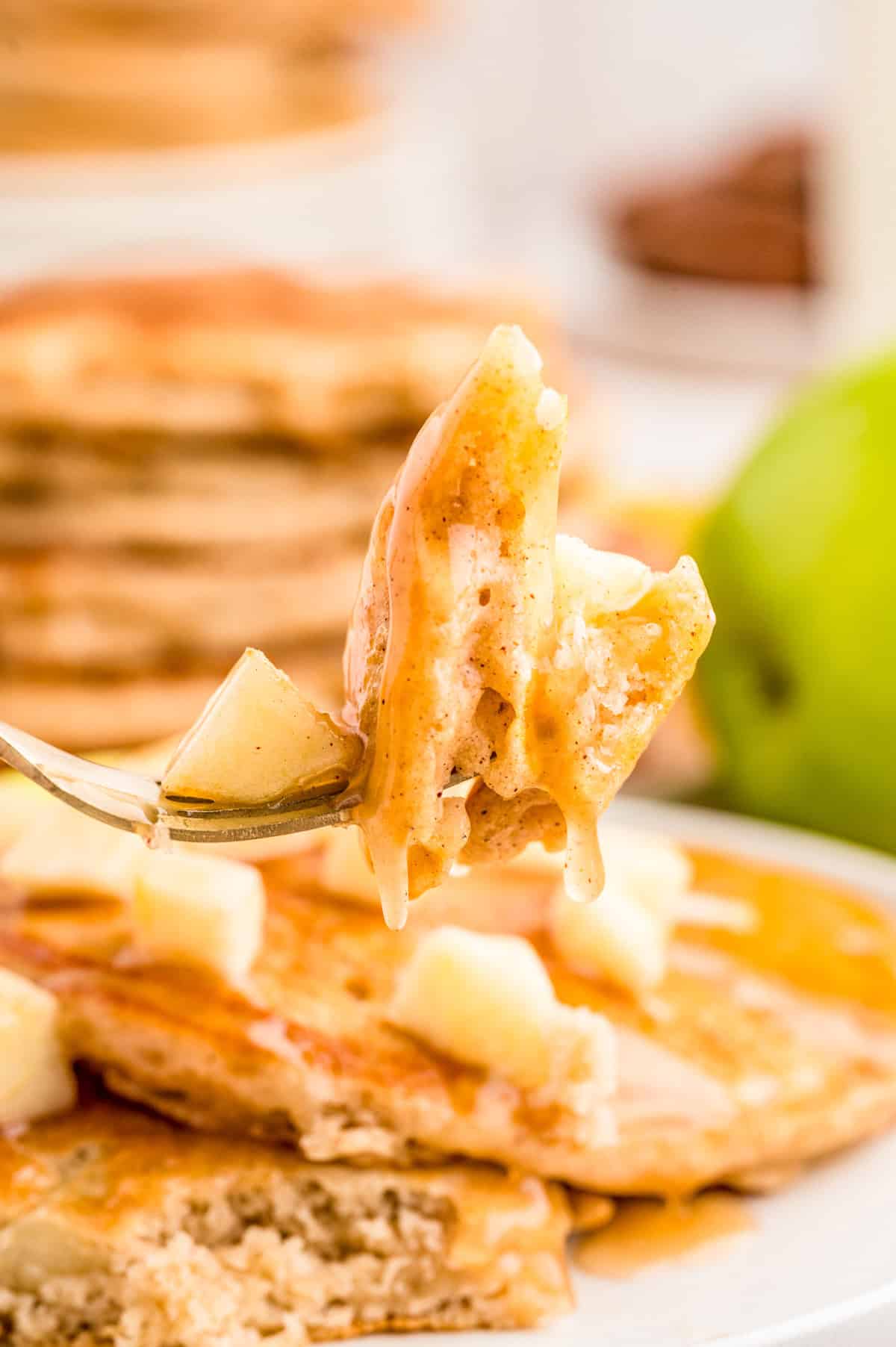 Fork holding up a bite of pancakes cut from the stack.