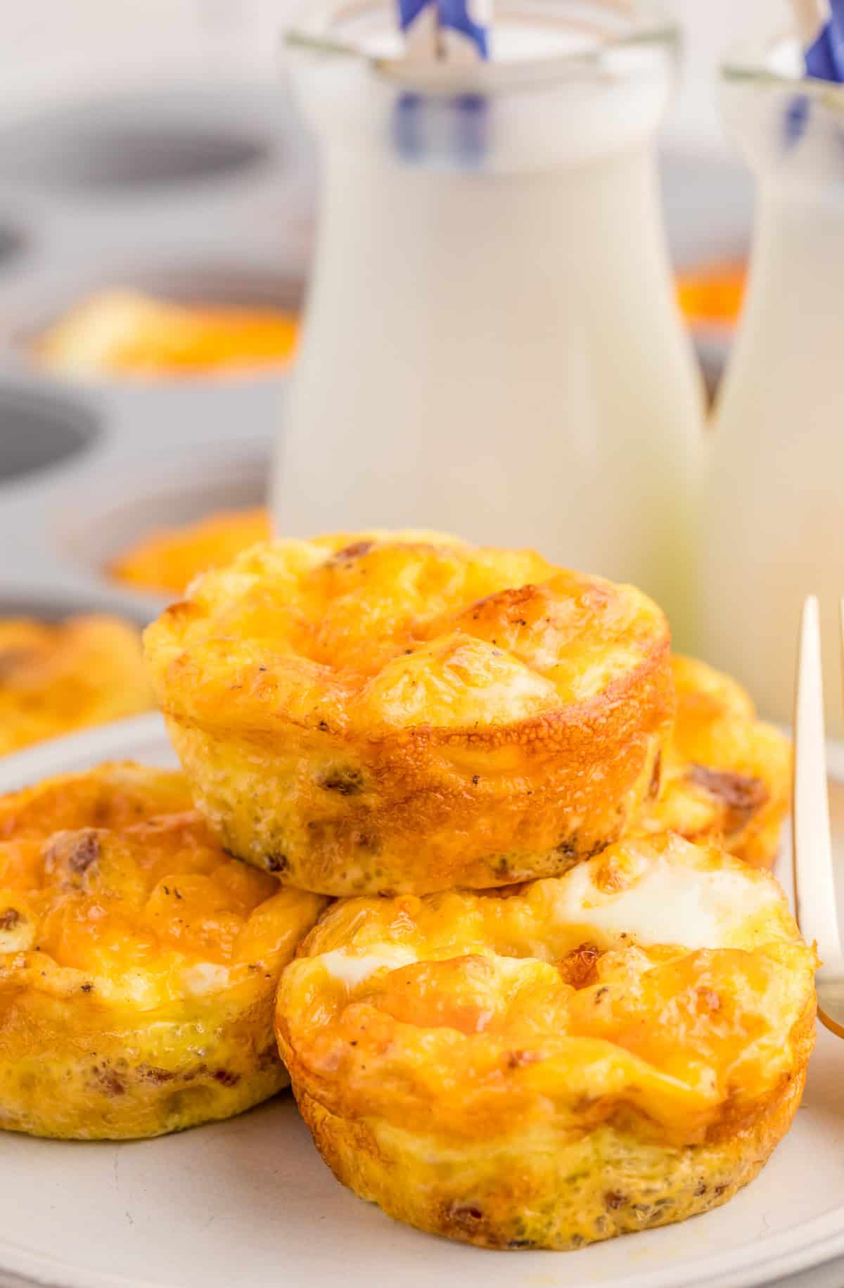 Bacon & Cheese Egg Bites stacked on white plat with milk in background.