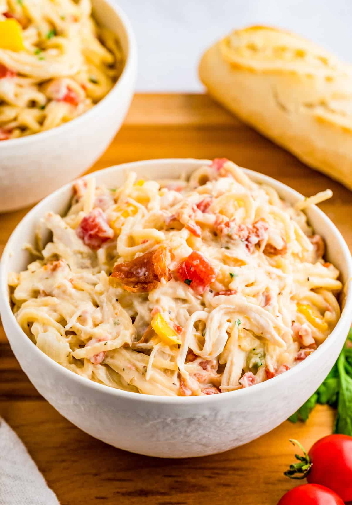 Chicken Spaghetti in white bowl on wooden board with bread in background.