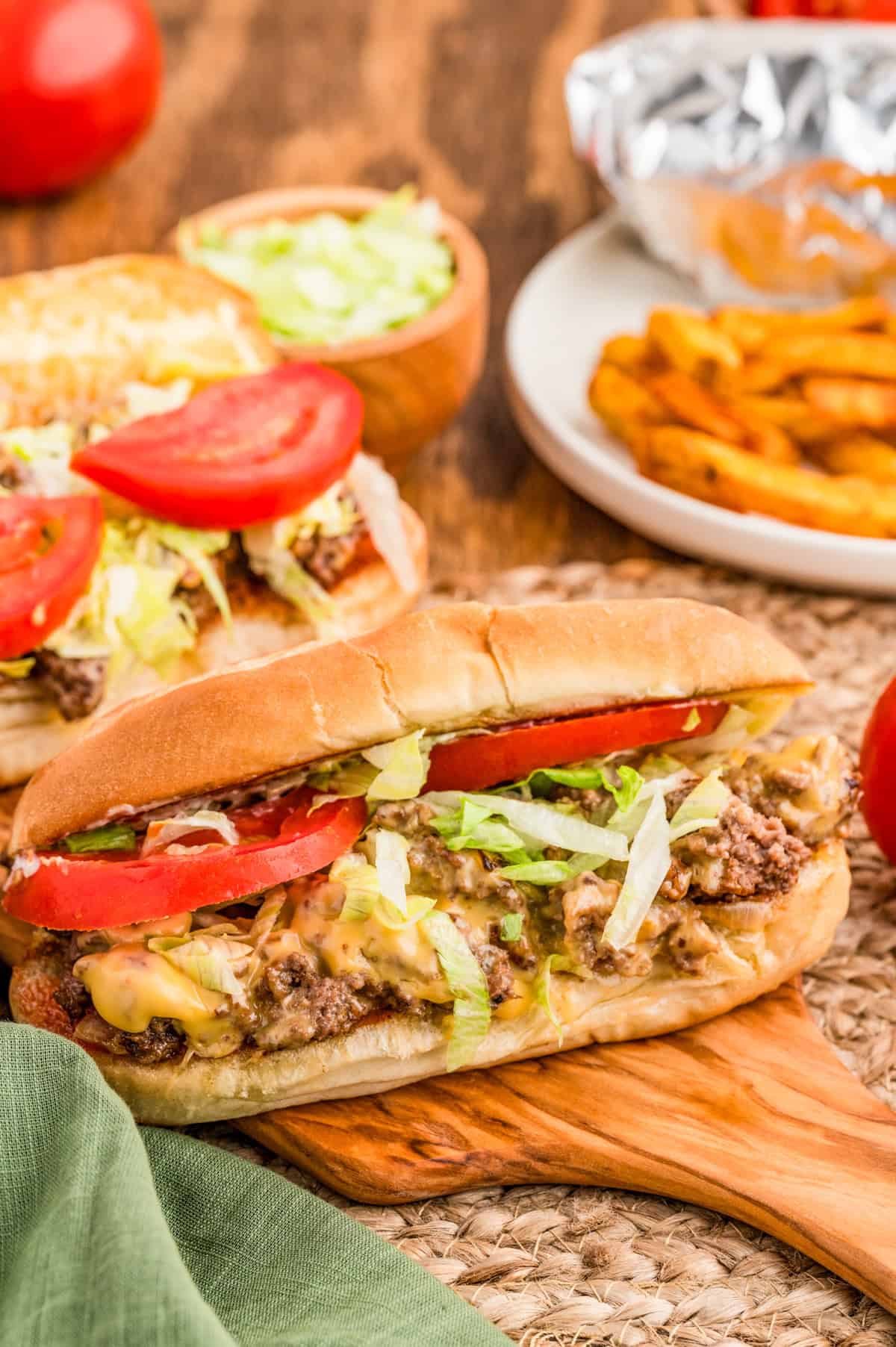 Chopped Cheese Sandwich on wooden board showing all the toppings with another sandwich in background.