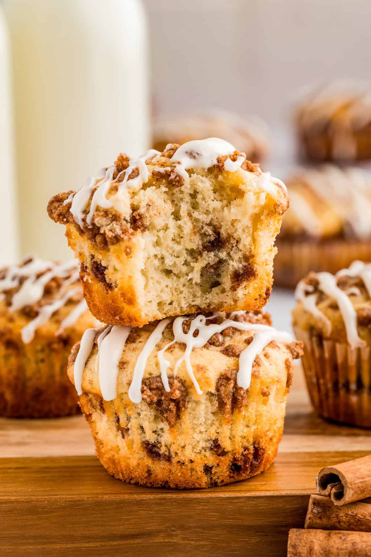 Two stacked Cinnamon Roll Muffins on wooden board with a bite taken out of the top muffin.