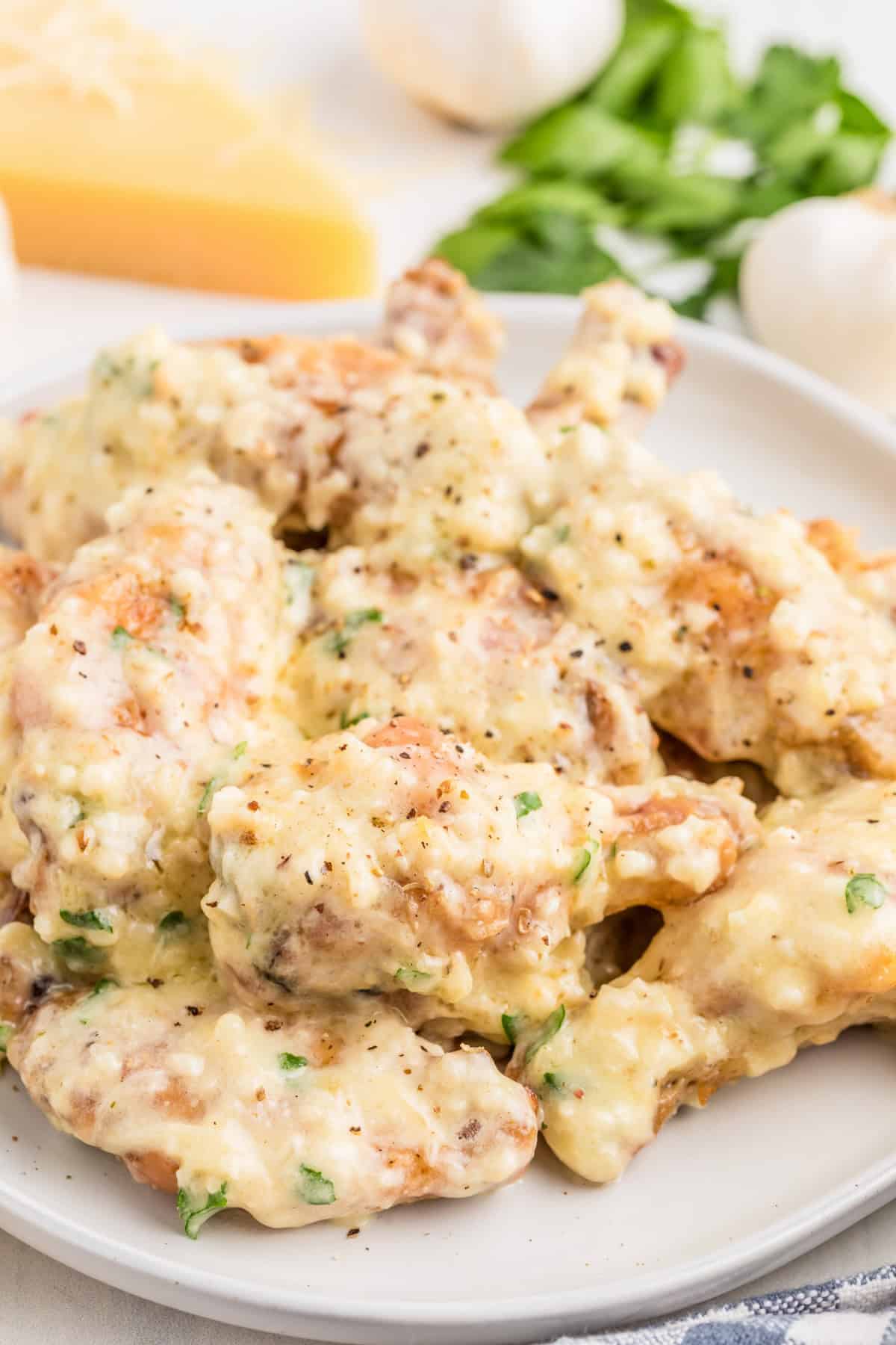 Garlic Parmesan Wings on white plate glazed in sauce with cheese and parsley in background.