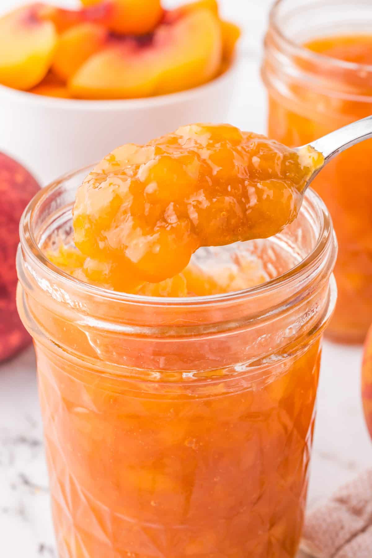 Homemade Peach Jam in mason jar with spoon holding up some jam out of jar.