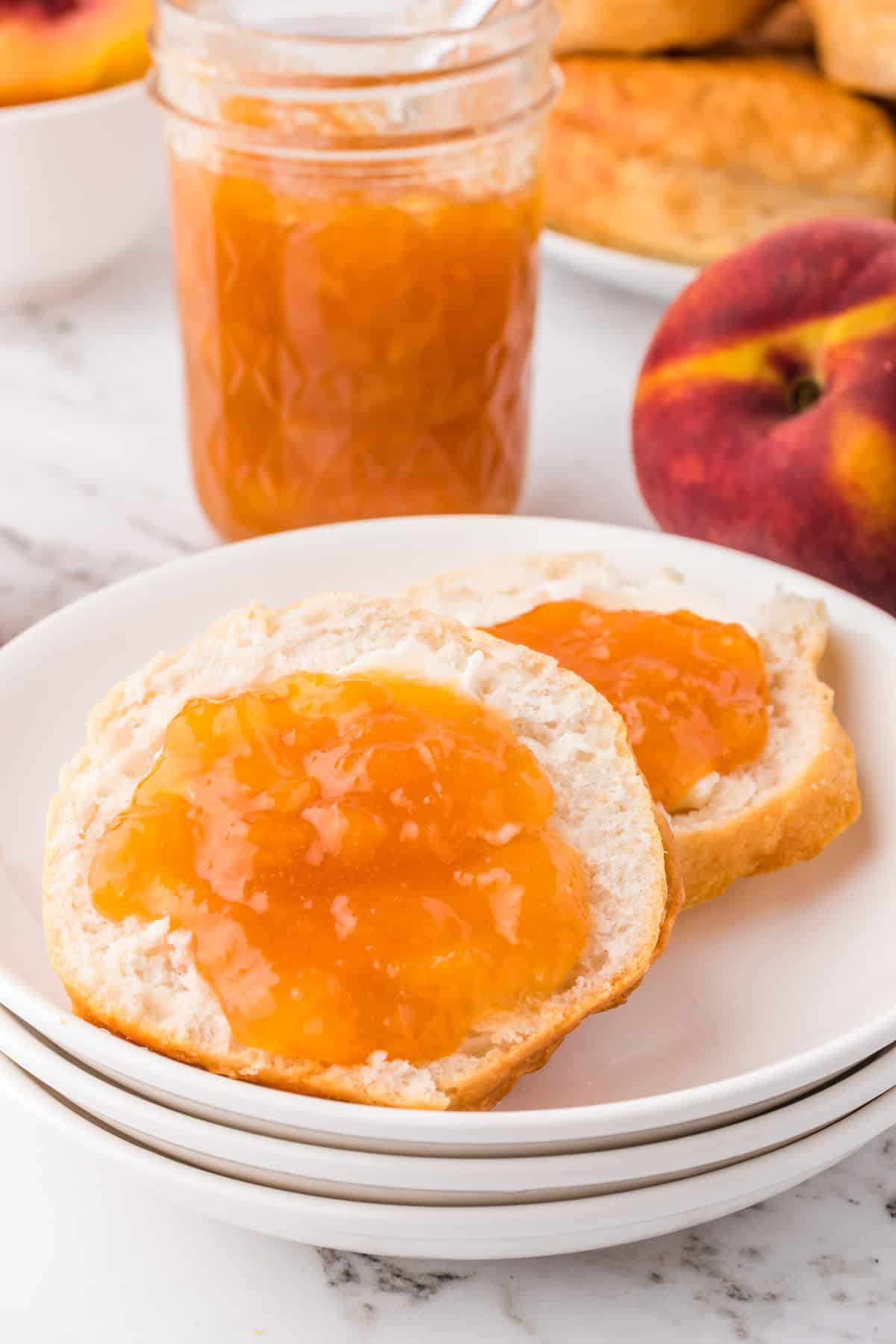 Peach Jam on muffins on white plate with jam in jar in background.