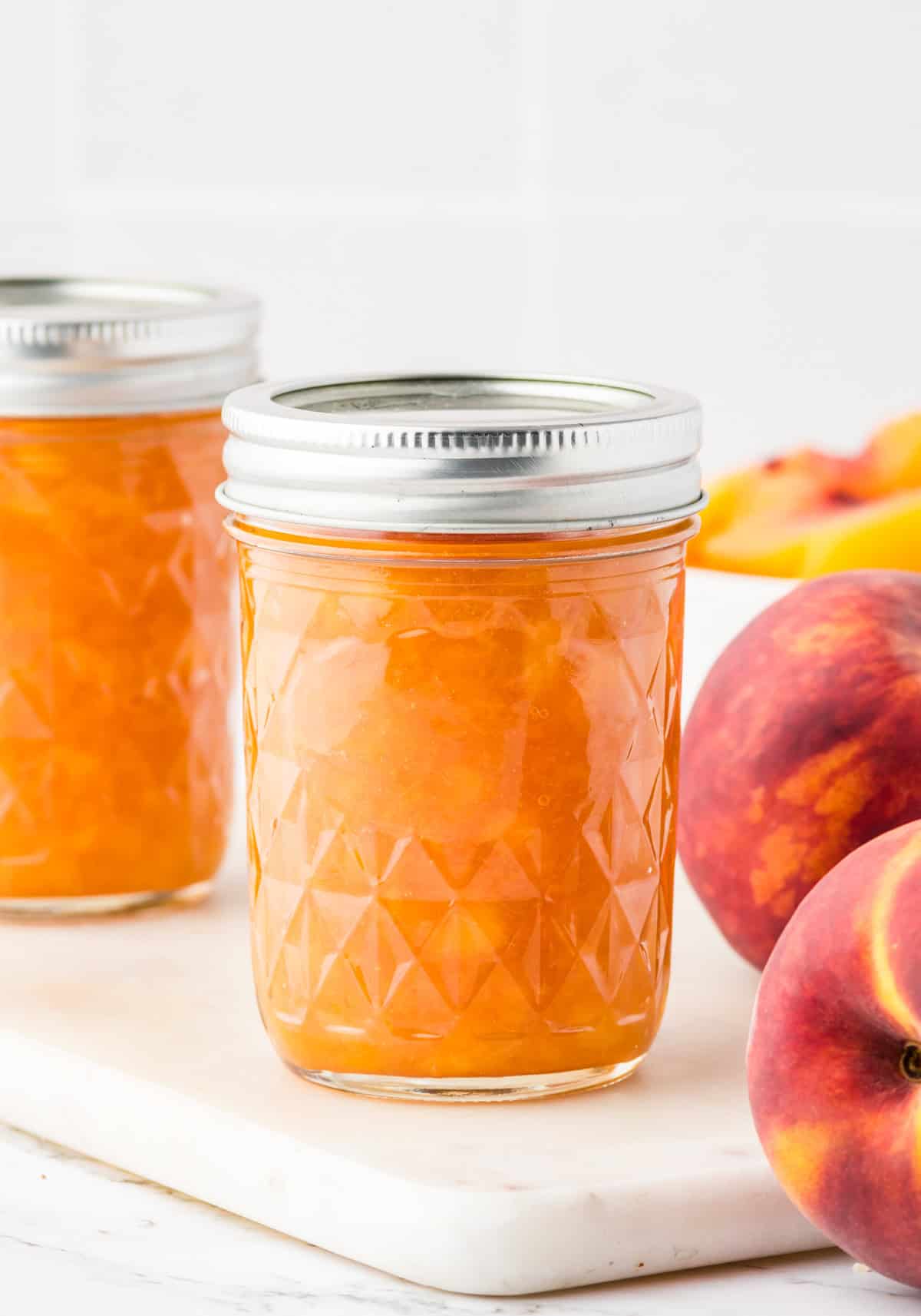 Finished Jam in mason jars next to peaches.